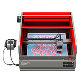 The CrealityFalcon Falcon2 Pro 22W/40W Enclosed Laser Engraver and Cutter is actively printing a detailed design. The machine has a red protective enclosure, a control panel at the front, and a power supply box connected to the left side, ensuring precise positioning and FDA Class 1 safety standards.