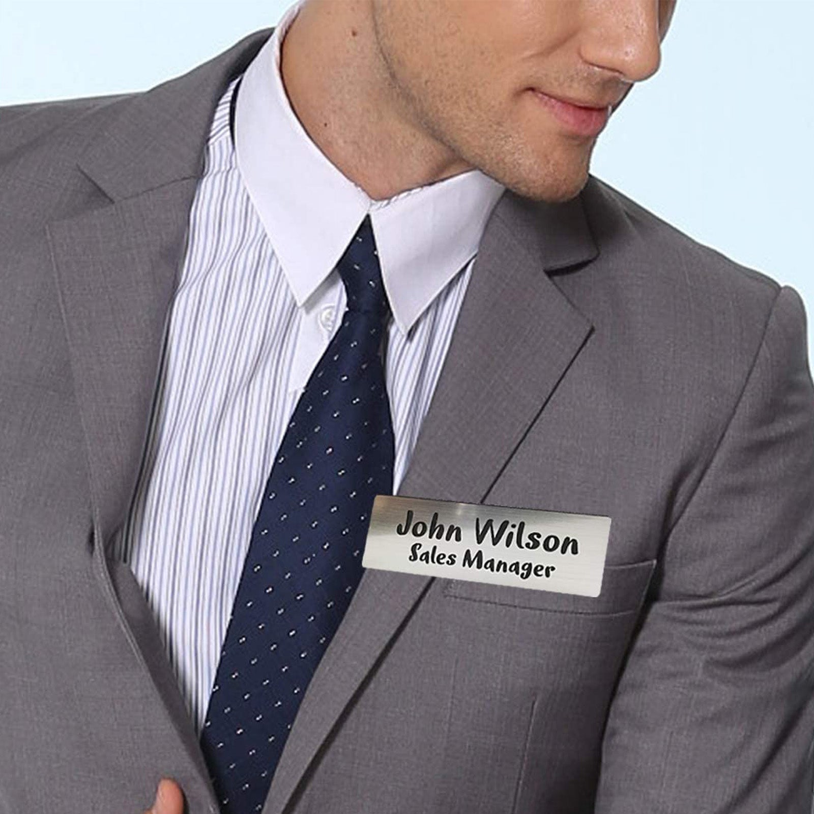 Two rectangular name badges are pictured, showcasing laser engraving ideas using CrealityFalcon's Titanium Steel Blank Stamping Tags for Engraving. The top badge is gold with a stag logo and the name "Barrett" engraved. The bottom badge is silver, created using a laser engraver for metal, featuring the name "John Wilson" and the title "Sales Manager" printed in black text.