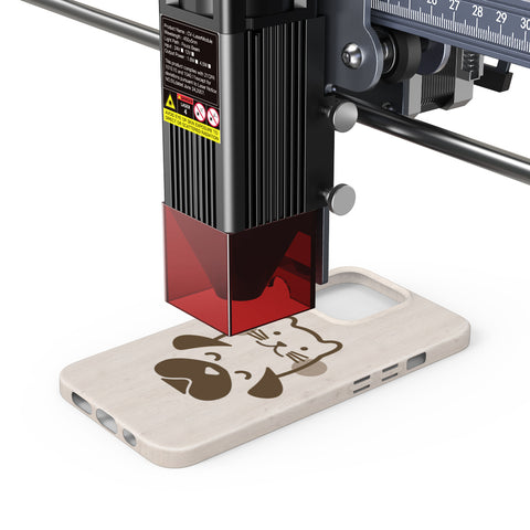 The CR-Laser Falcon 7.5W Laser Engraver by CrealityFalcon, equipped with a red protective shield, is etching a design of a cat and dog face onto a beige smartphone case. The detailed process demonstrates precision engraving on the case's surface.