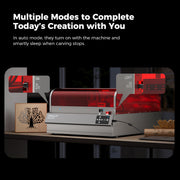 A laser engraving machine with a red protective cover, labeled "CrealityFalcon," is shown on a desk under the text "Multiple Modes to Complete Today's Creation with You." The Falcon2 Pro 22W/40W Enclosed Laser Engraver and Cutter is surrounded by small wooden art pieces and has labels for "FAN" and "LIGHT" with "AUTO" settings. Featuring safety certification, it ensures peace of mind during use.
