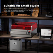 A compact Creality Falcon2 Pro 60W Enclosed Diode Laser Engraver with Class 1 safety and a red protective cover sits on a studio shelf, surrounded by wooden engravings, a laptop with design software, and another Creality device below.