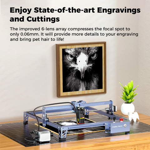 An engraving machine on a table, in front of a wall displaying an intricate black and white eagle engraving. Text in the top left corner reads: "Enjoy State-of-the-art Engravings and Cuttings with CrealityFalcon Falcon Pro 10W Laser Engraver." A green plant is seen beside the laser engraver on the table.